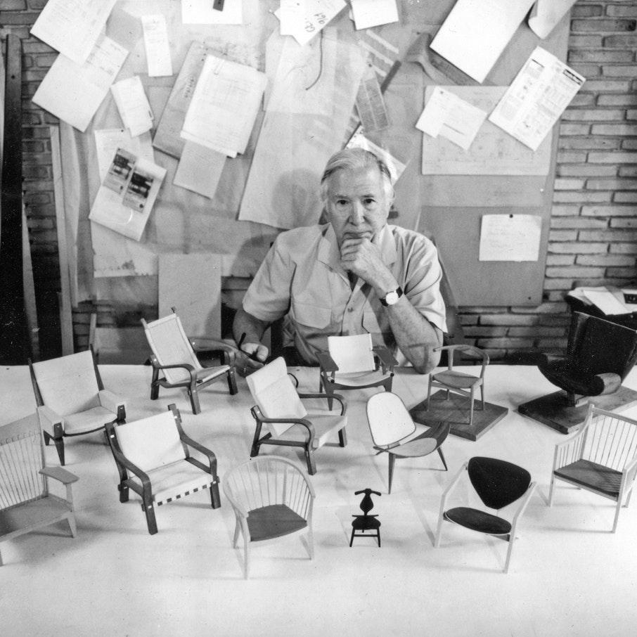 Hans Wegner seated at a table with scale models of his chair designs